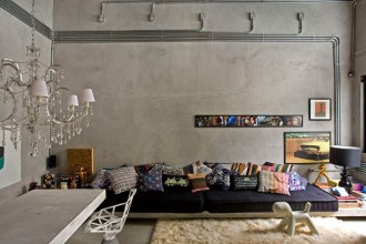 Il divano è formato da un piano in cemento che occupa tutta la parete del living su cui sono appoggiati due larghi materassi neri completamente coperti dai cuscini in tessuto stampato