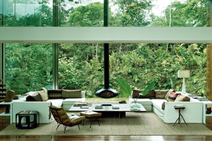 Le grandi vetrate proiettano l’ambiente del living nella foresta con un effetto scenografico. Rigorosi divani bianchi incorniciano il tappeto del designer brasiliano Nani Chinellato. La poltrona con poggiapiedi anni 60 è un pezzo di famiglia