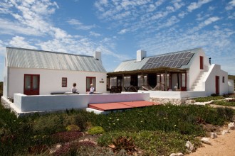 Nell’immagine del cottage sono visibili i pannelli fotovoltaici sulla falda del tetto esposta a nord e i portelli rossi della cisterna sotterranea per la raccolta dell’acqua piovana